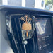 A wooden flower-shaped car air freshener with three flowers and a clear glass bottle filled with amber liquid, clipped onto a car dashboard air vent next to the infotainment screen.
