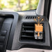 A car air freshener with a wooden flower stem and glass bottle placed on a vehicle's dashboard air vent.