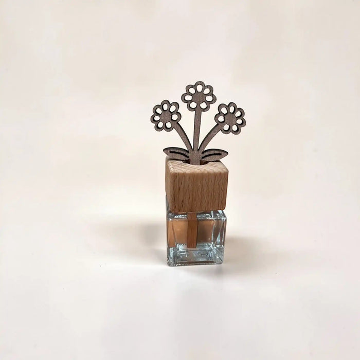 A small decorative object with a clear glass base, a light wood cap, and a metal flower-shaped top, photographed on a plain light background.
