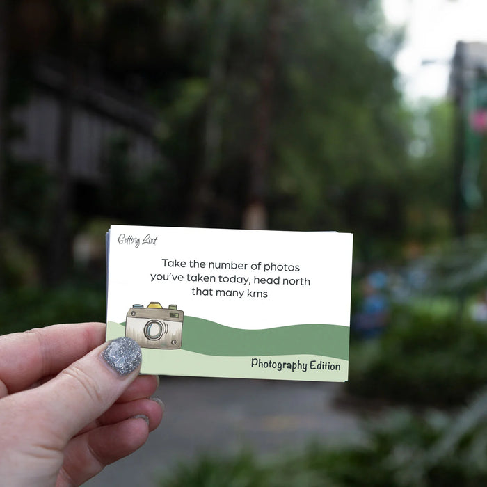 Hand holding a card with text and a camera illustration, blurred green outdoor background