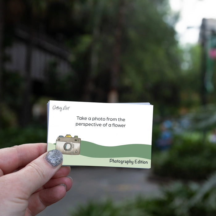 Hand holding a card with a camera illustration and text, blurred outdoor background