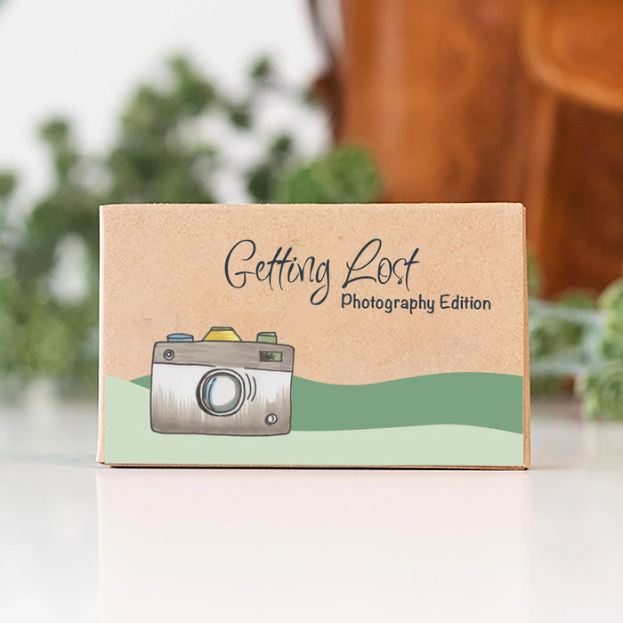 Box with 'Getting Lost Photography Edition' text and camera illustration on a blurred natural background