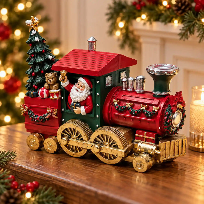 A decorative Christmas steam train figurine sits on a wooden table in a warmly lit holiday setting. The train is primarily red and dark green with gold-toned wheels and trim, featuring Santa Claus in the driver's seat, a small Christmas tree, a teddy bear, and gift boxes.