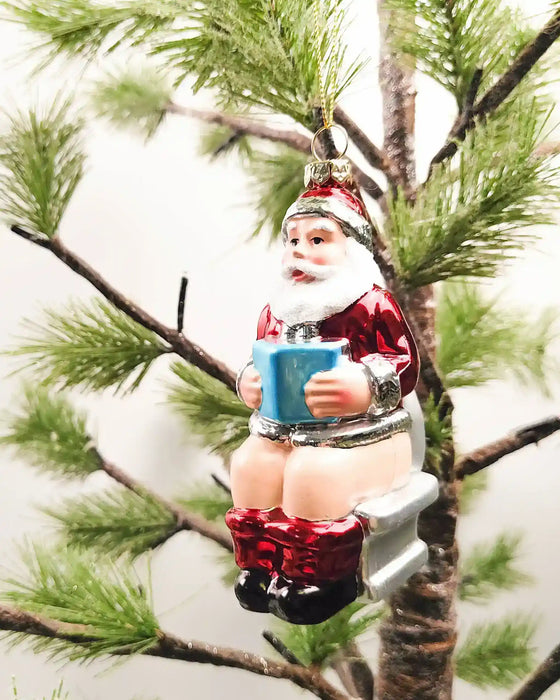 Santa on toilet novelty glass Christmas ornament with red suit and boots, hanging on a tree