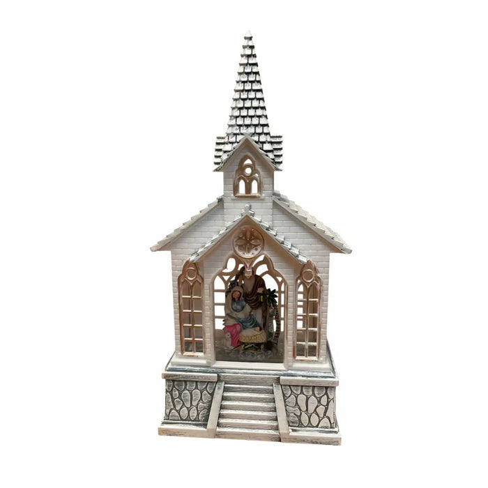 A miniature church-shaped nativity display with a white and gray facade, a gray shingled steeple, and a small interior figurine of the Holy Family visible through arched windows, set against a plain white background.