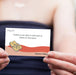 Hand holding a card with text and a flip-flop illustration, with a blurred background.