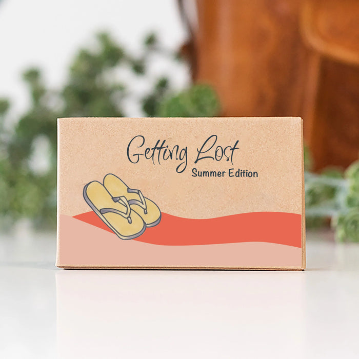 Kraft paper box with flip-flop illustration and 'Getting Lost Summer Edition' text on a blurred background