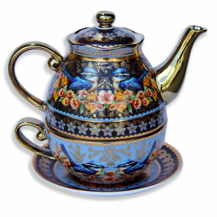 A decorative porcelain teapot with a matching saucer and cup, featuring blue birds, colorful flowers, and gold detailing on a white background.