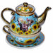 An ornate ceramic tea-for-one set featuring a teapot stacked on a matching cup and saucer, decorated with a highland cow, sunflowers, daisies, bees, and gold honeycomb detail on a sky blue background with gold trim