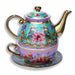 An ornate ceramic teapot with a matching saucer and cup, decorated with intricate floral and bird motifs on a light purple background with gold trim.
