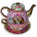 A pink and gold porcelain tea for one teapot with a matching cup and saucer, decorated with a whimsical Wonder Wombat illustration wearing pink glasses and a bow, on a white background.