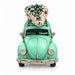 A vintage mint green toy or decorative Volkswagen Beetle car with a small frosted Christmas tree on its roof rack, photographed against a plain white background.