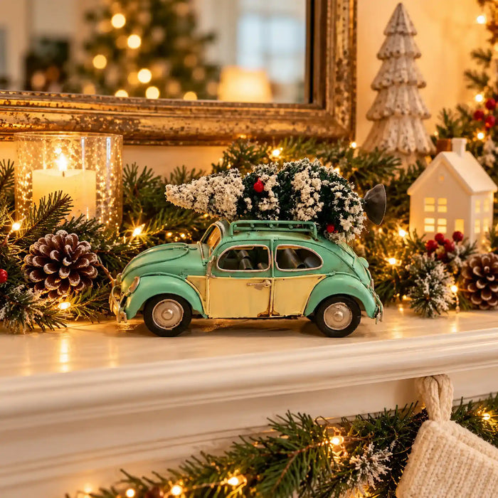 A vintage-style toy car in mint green and cream sits on a decorated Christmas mantel with pinecones, evergreen garland, warm string lights, candles, and holiday decor in the background.
