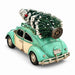 A vintage-style teal and cream toy car with a small Christmas tree strapped onto the roof rack, photographed on a clean white background.