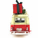 A vintage toy or model van with a cream upper body and red lower body, shown from the rear. A large red gift box with a dark green ribbon is strapped to the roof rack, and a small green box is visible on the right side.