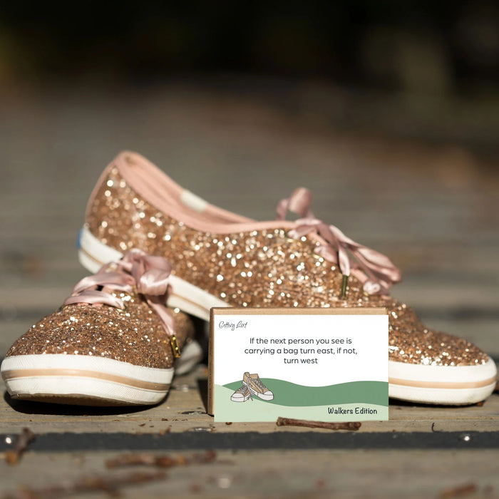 Gold glittery shoes with pink laces on a wooden surface, accompanied by a card.