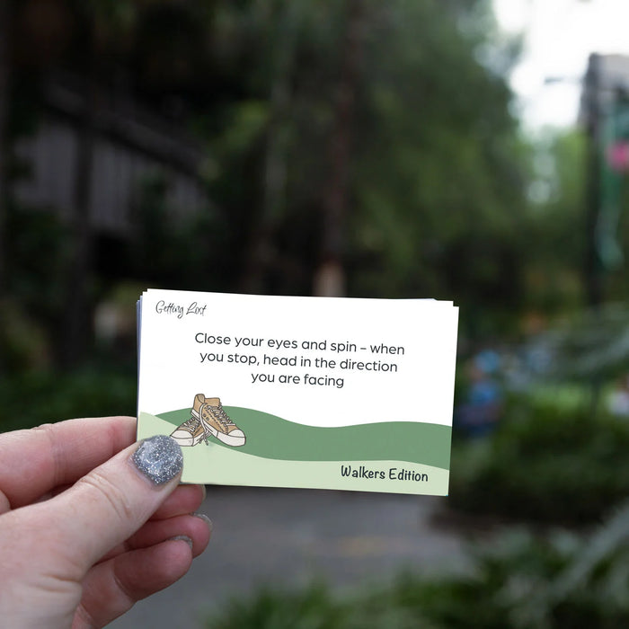 Hand holding a card with text and a shoe illustration against a blurred outdoor background