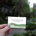 Hand holding a card with text and a shoe illustration against a blurred outdoor background