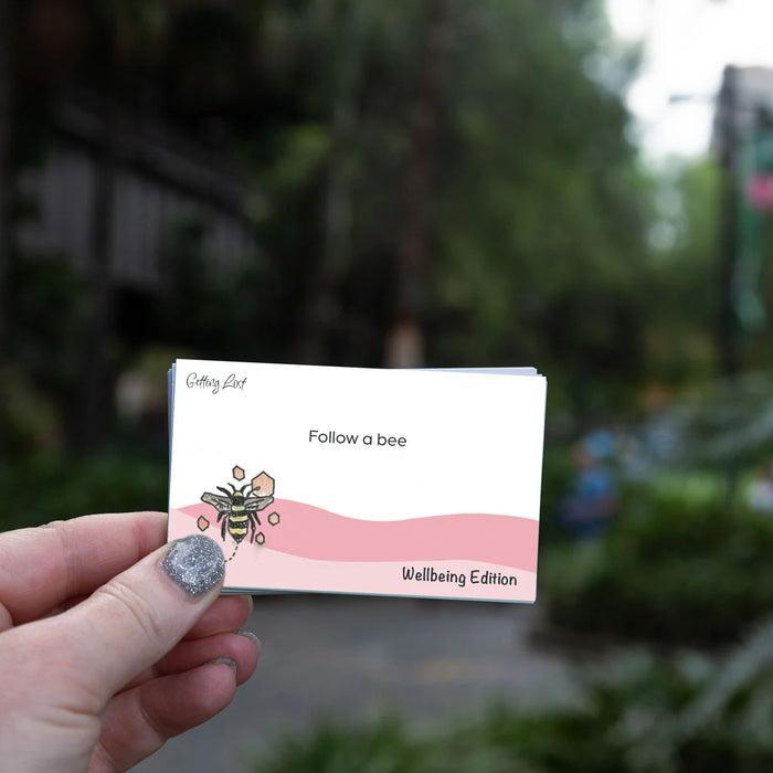 Hand holding a card with a bee illustration and text 'Follow a bee' in an outdoor setting.