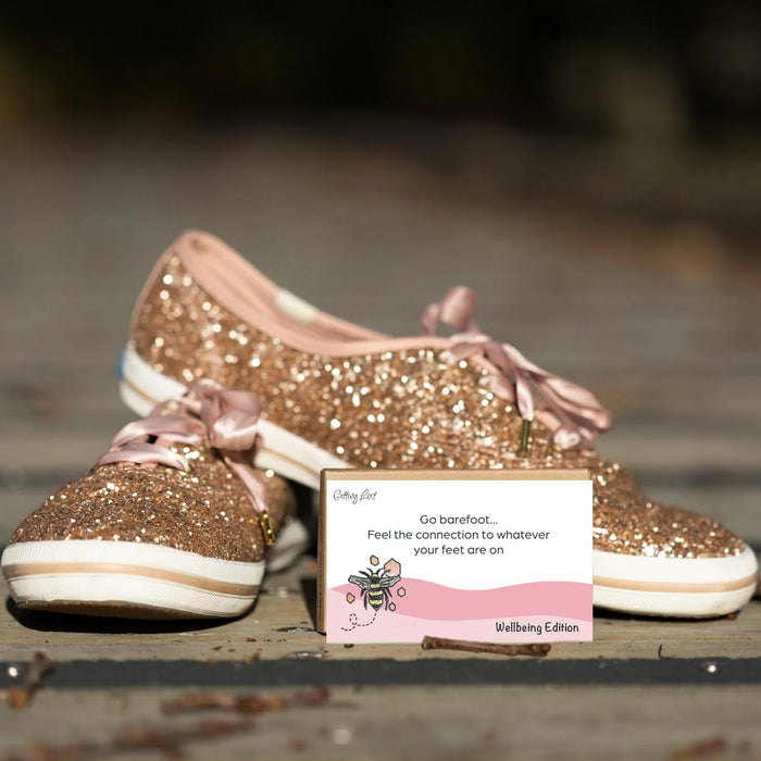 Glittery gold shoes with pink laces on a wooden surface, accompanied by a card.