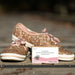 Glittery gold shoes with pink laces on a wooden surface, accompanied by a card.