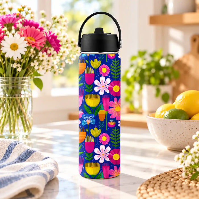 Wild Joy 620ml insulated water bottle with bright floral artwork on blue, styled on a kitchen bench beside flowers and citrus fruit.