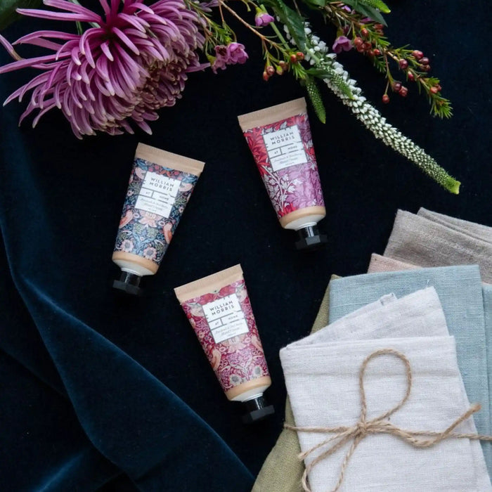 Three hand cream tubes with floral designs on a dark surface with folded fabric and flowers.