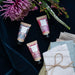 Three hand cream tubes with floral designs on a dark surface with folded fabric and flowers.
