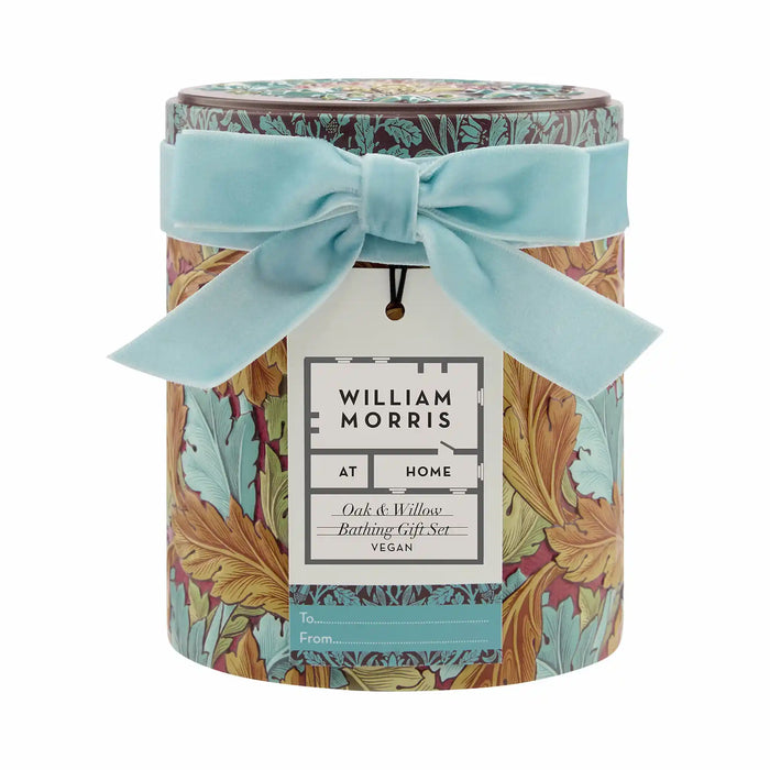 William Morris 'At Home' Bathing Gift Set in a round tin container with a light blue velvet ribbon bow and a hanging paper tag, on a white background.