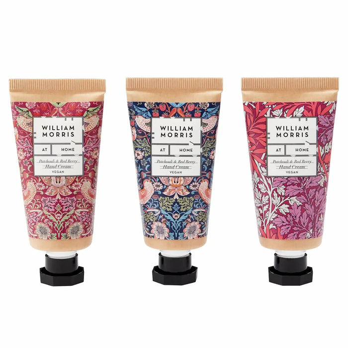 Three William Morris 'At Home' hand cream tubes with black caps, displayed side-by-side against a white background. Each tube features a different botanical pattern: a pink damask on the left, a blue floral on the center, and a pink botanical on the right.