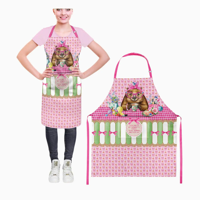 A pink novelty apron with a cartoon koala design, shown both worn by a model and as a flat product layout. The apron features a pink and green gingham top section, a green and white striped middle band, and a pink patterned bottom section with a central round badge.