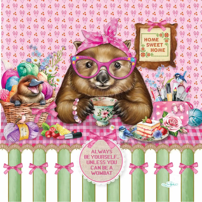 A whimsical illustrated scene featuring a brown wombat wearing pink glasses and a pink bow headband, sitting at a table with a teacup and surrounded by colorful craft supplies, flowers, yarn, and a sign that reads 'Home Sweet Home.' A smaller wombat appears in a basket on the left.